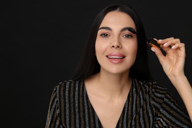 Photo of Beautiful young woman applying mascara on black background, space for text