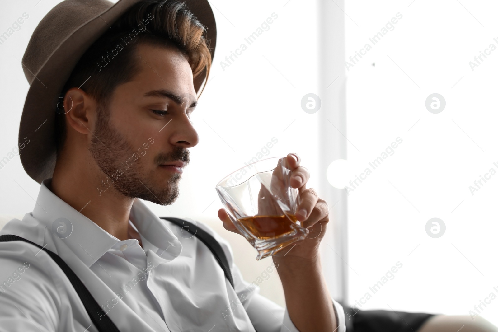 Photo of Young man with glass of whiskey at home. Space for text