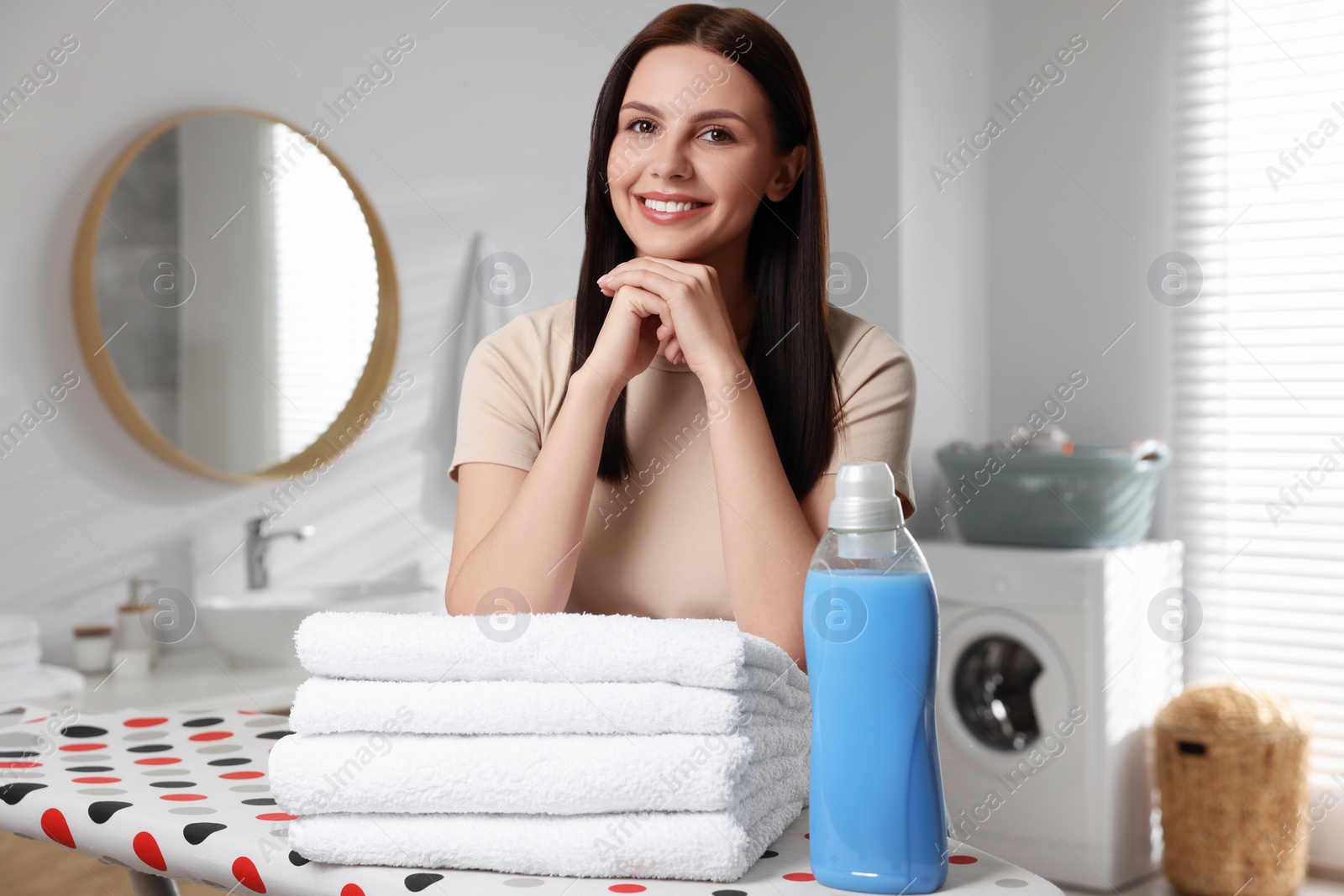 Photo of Woman near fabric softener and clean towels in bathroom