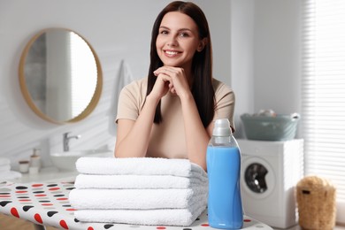 Photo of Woman near fabric softener and clean towels in bathroom
