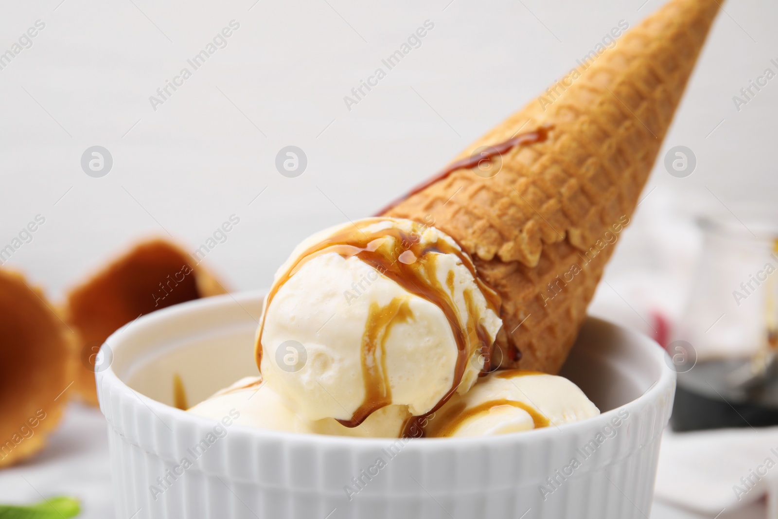 Photo of Scoops of ice cream with caramel sauce and wafer cone in bowl, closeup