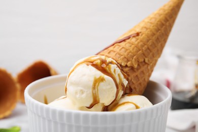 Photo of Scoopsice cream with caramel sauce and wafer cone in bowl, closeup