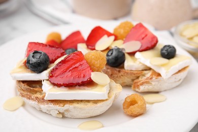 Photo of Tasty sandwiches with brie cheese, fresh berries and almond flakes on white plate, closeup