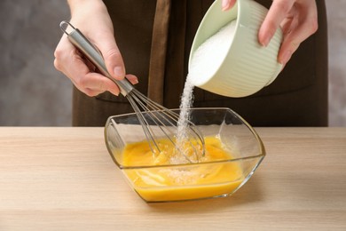 Photo of Woman adding sugar to whisked eggs at wooden table, closeup