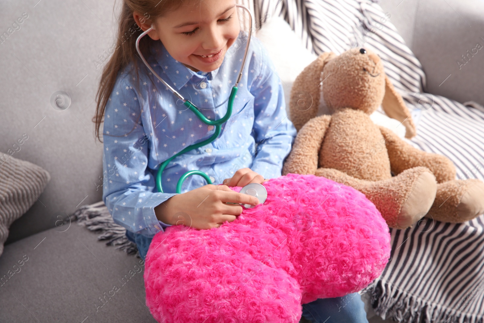 Photo of Cute child imagining herself doctor while playing with stethoscope on sofa in living room