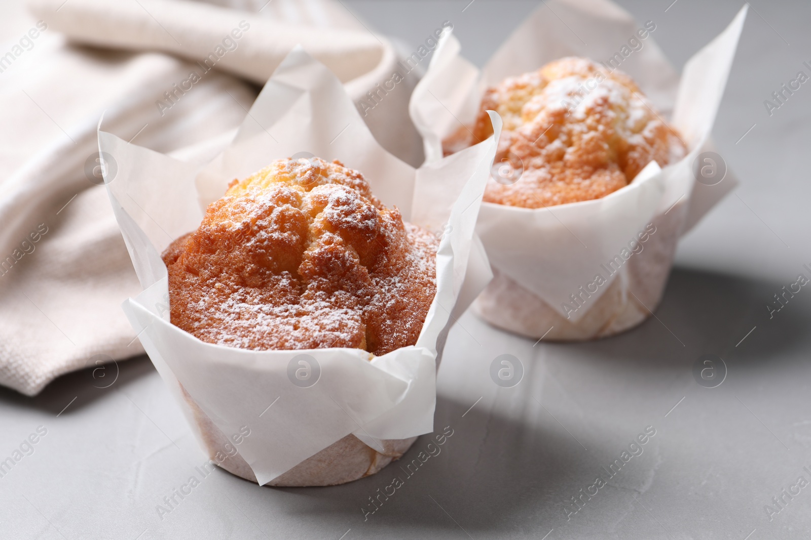 Photo of Delicious muffins with powdered sugar on light table, closeup