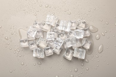 Pile of melting ice cubes and water drops on light grey background, flat lay