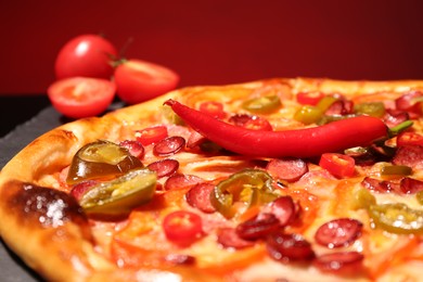 Photo of Delicious pizza Diablo, tomatoes and chili peppers against red background, closeup