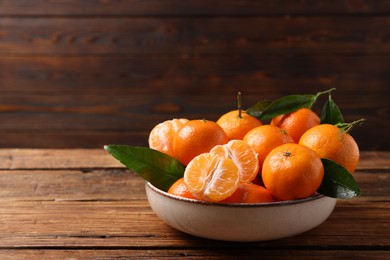 Fresh tangerines with green leaves in bowl on wooden table, space for text