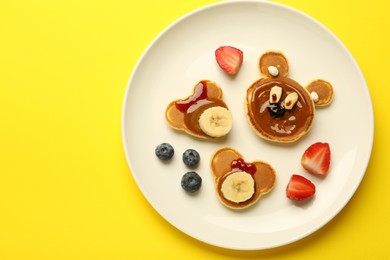 Creative serving for kids. Plate with cute bears made of pancakes, berries, banana and chocolate paste on yellow background, top view. Space for text