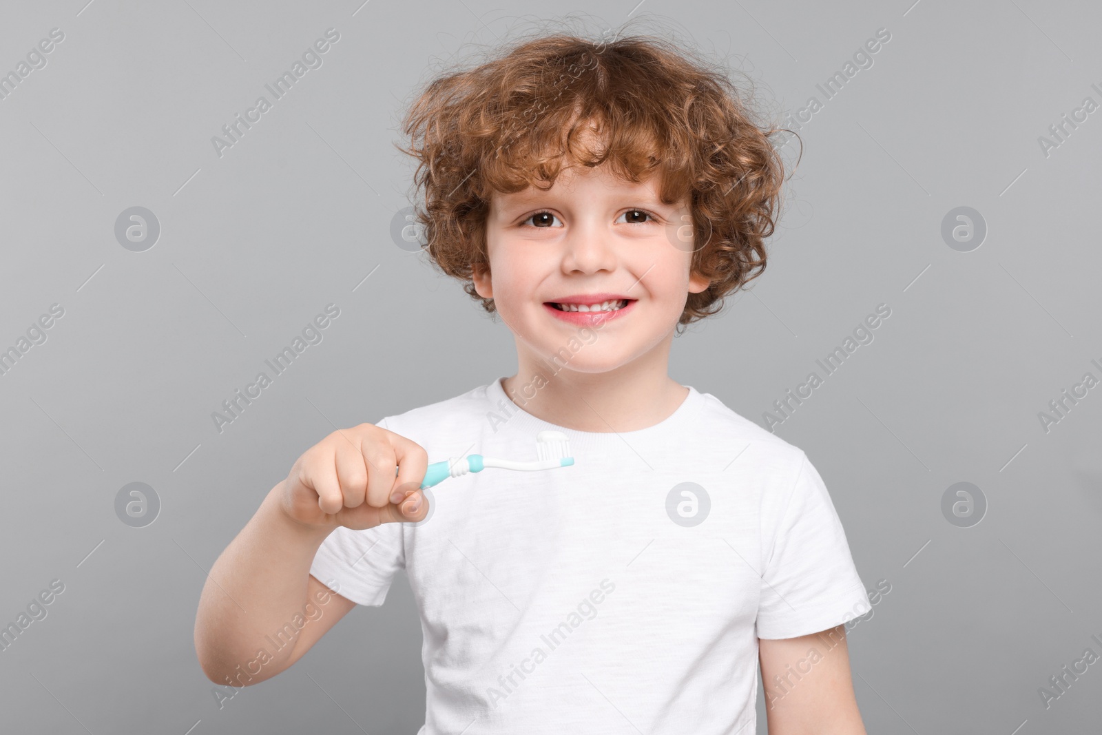 Photo of Cute little boy holding plastic toothbrush with paste on light grey background