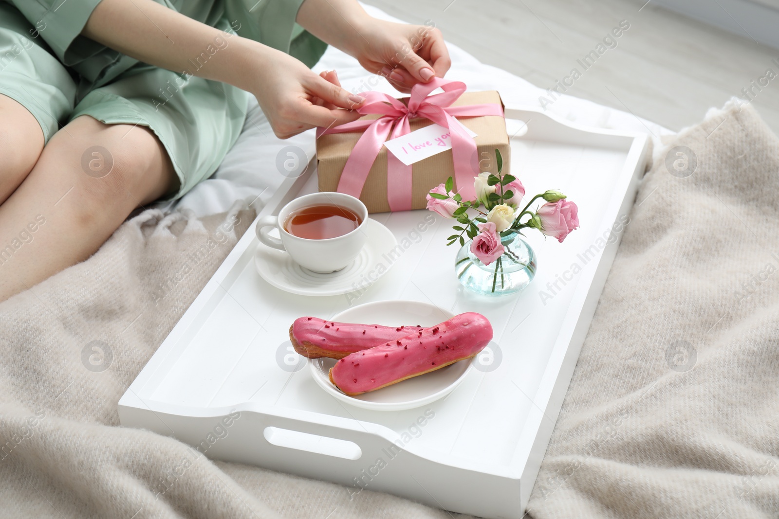 Photo of Tasty breakfast served in bed. Woman with gift box, tea, eclairs, flowers and I Love You card at home, closeup