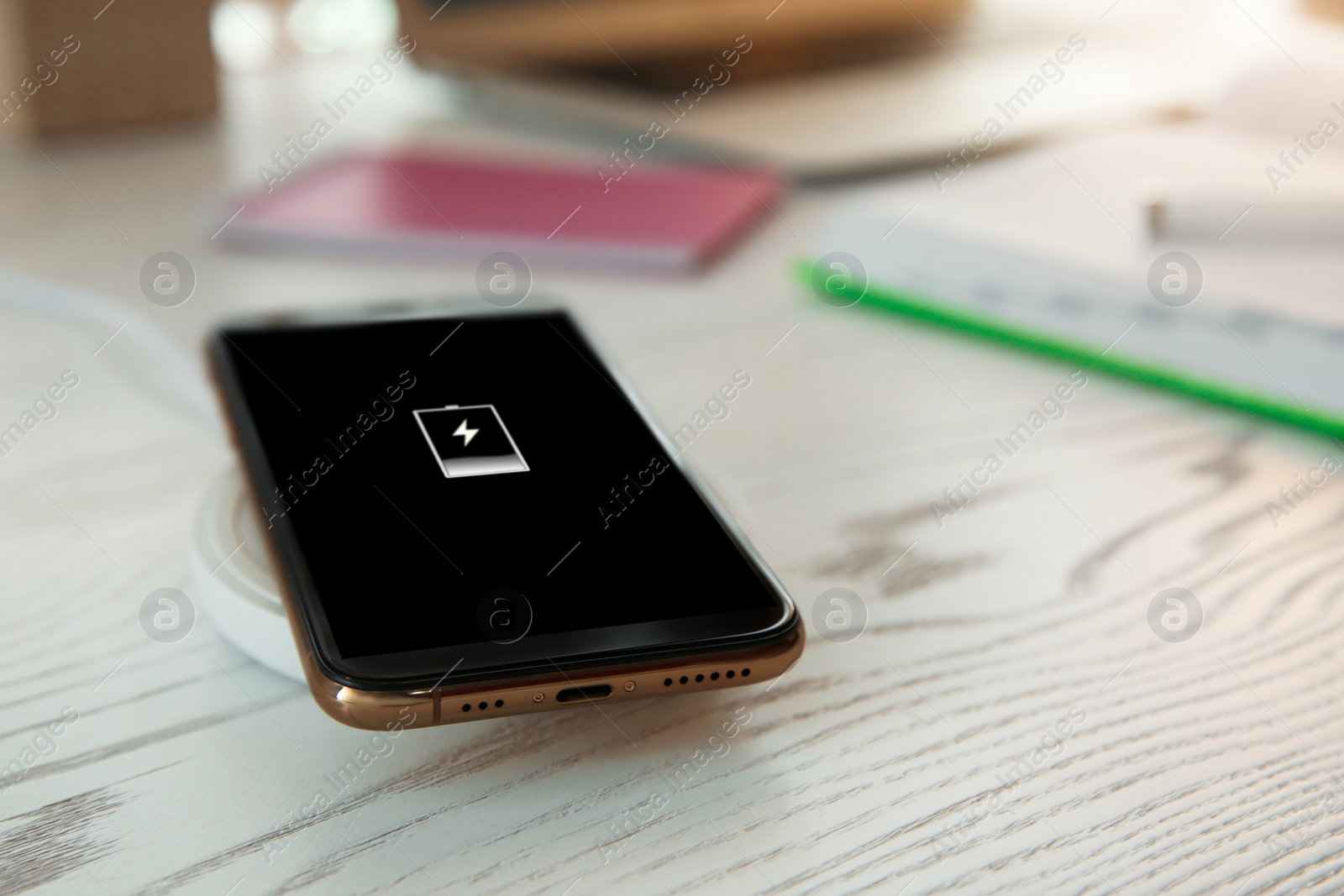 Photo of Mobile phone with wireless charger on white wooden table. Modern workplace accessory