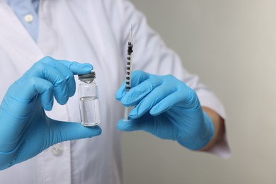 Doctor holding syringe and glass vial on grey background, closeup