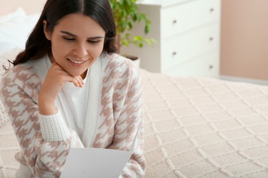 Photo of Young woman with greeting card on bed in room, closeup. Space for text