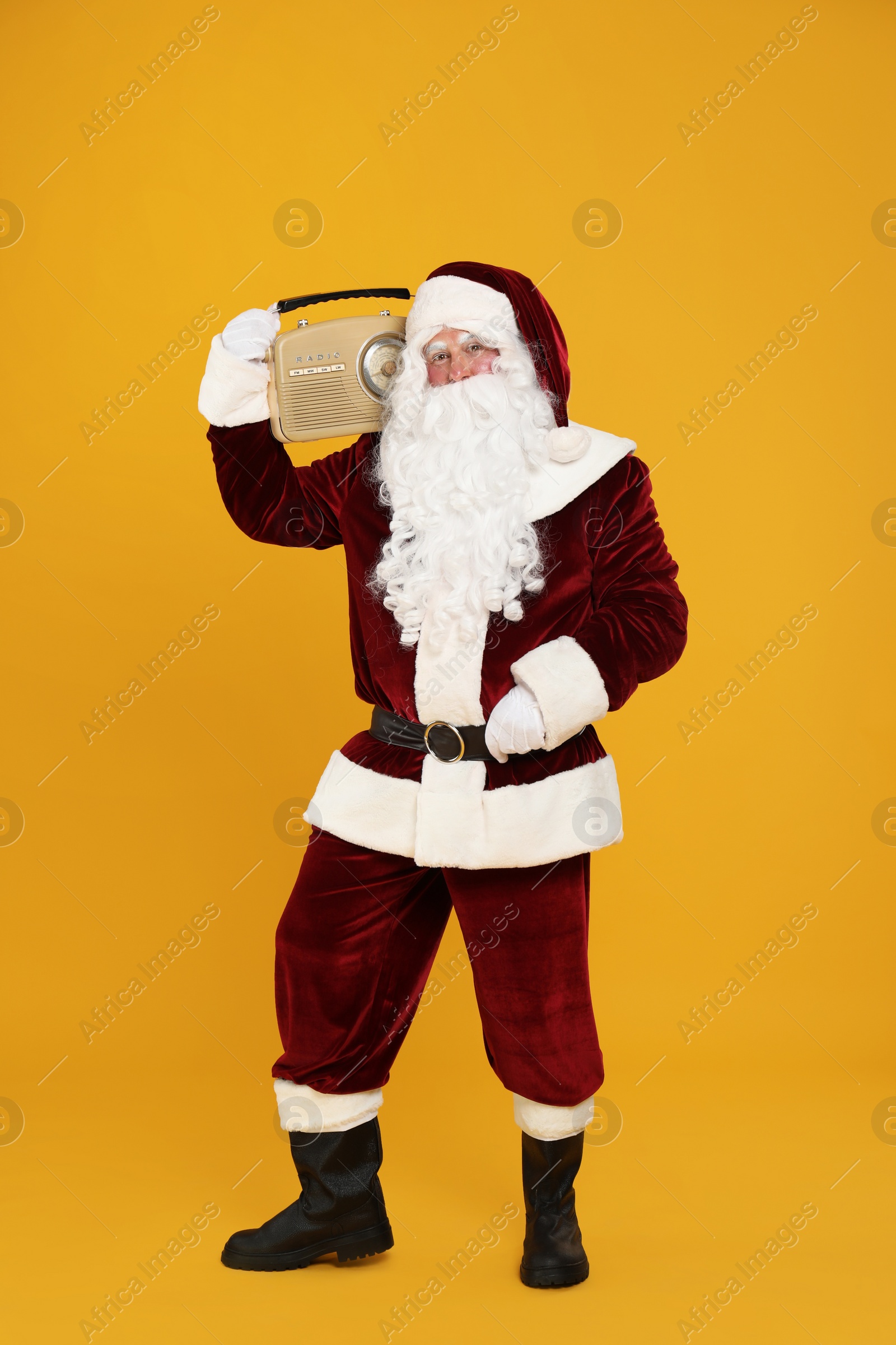 Photo of Santa Claus with vintage radio on yellow background. Christmas music