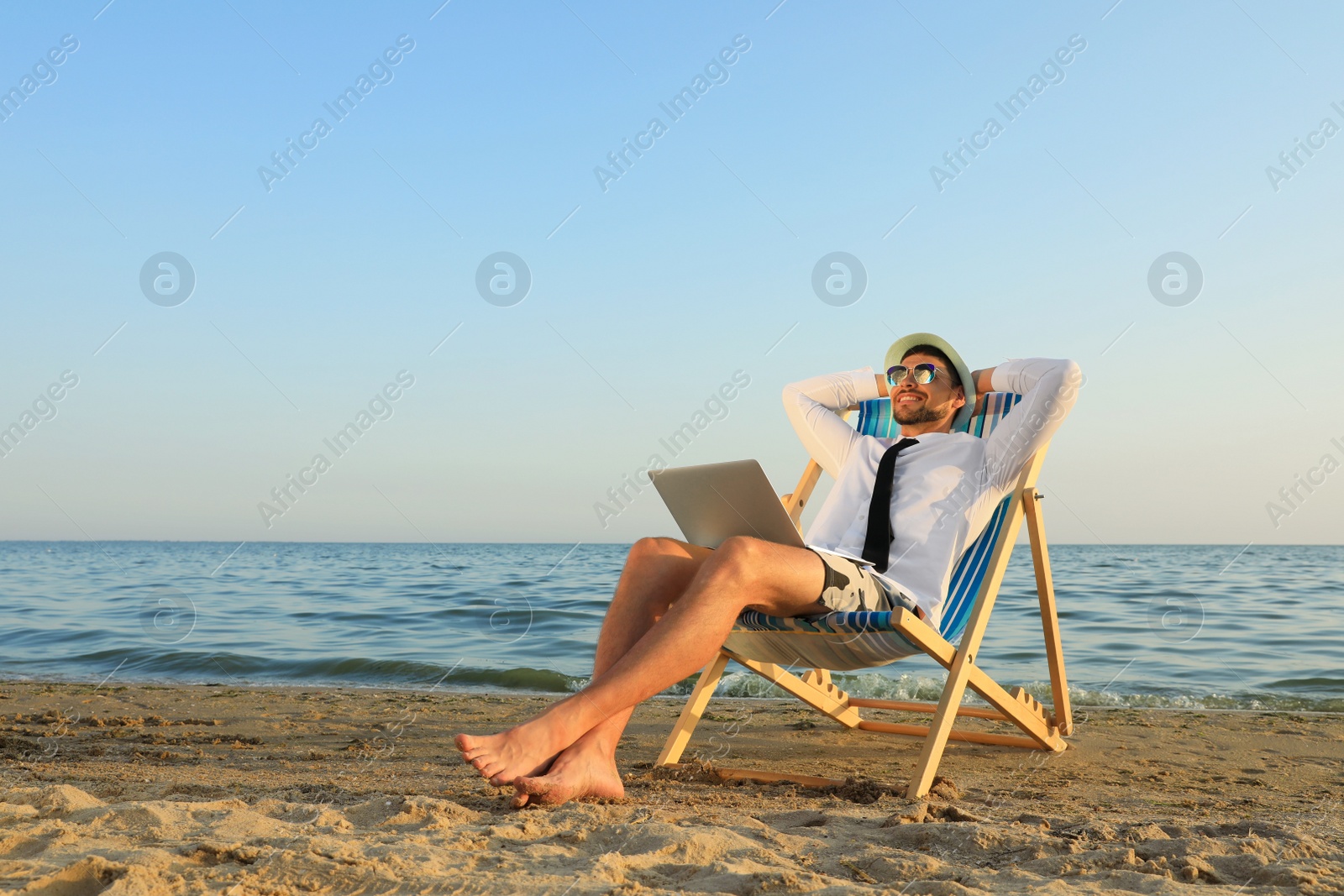 Photo of Happy man with laptop resting on deckchair near sea. Business trip