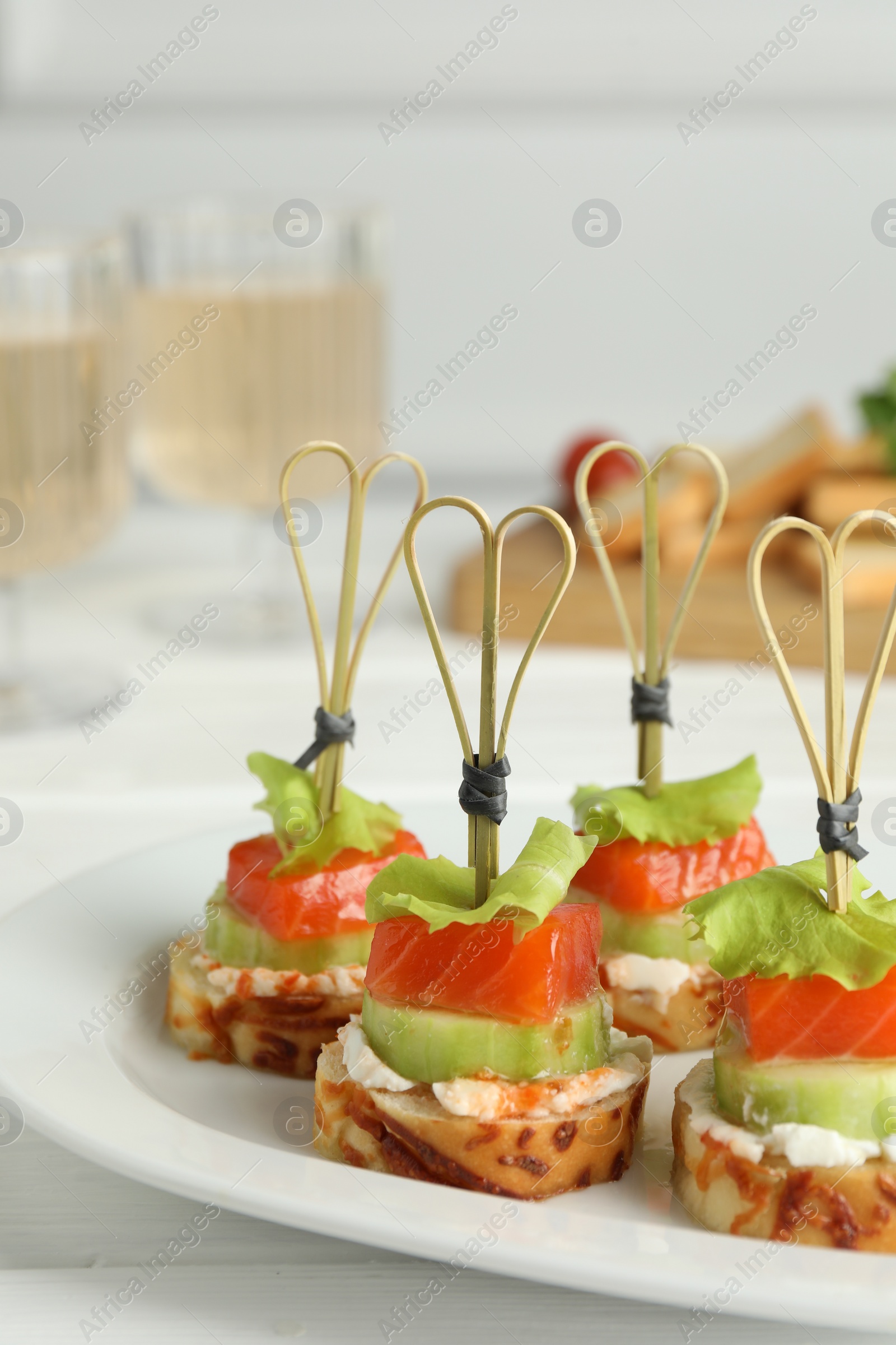 Photo of Tasty canapes with salmon, cucumber, bread and cream cheese on white table, closeup