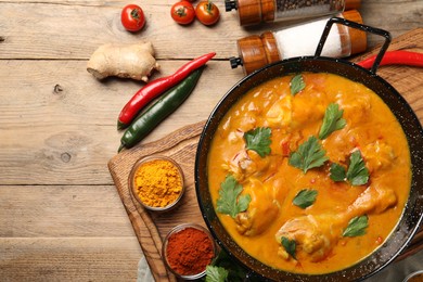 Photo of Tasty chicken curry with parsley and ingredients on wooden table, flat lay. Space for text
