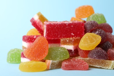 Photo of Pile of delicious bright jelly candies on light blue background, closeup