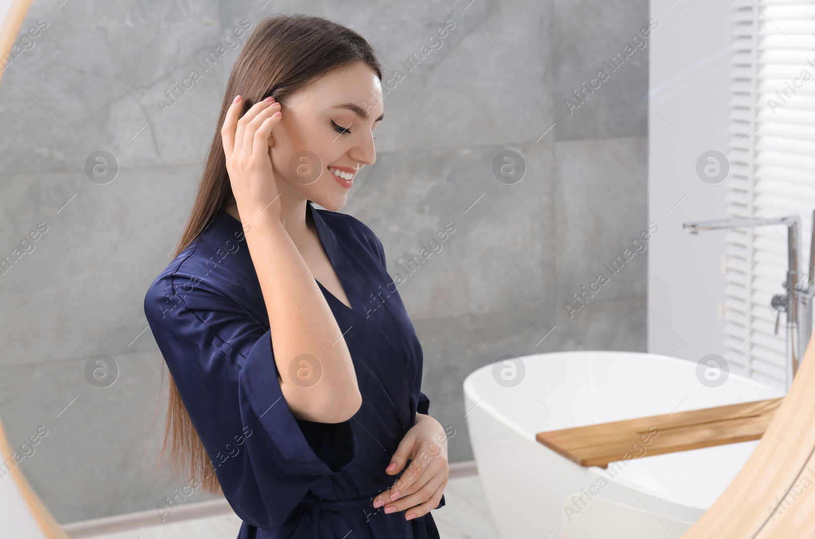 Photo of Beautiful woman in blue robe near mirror in bathroom, space for text