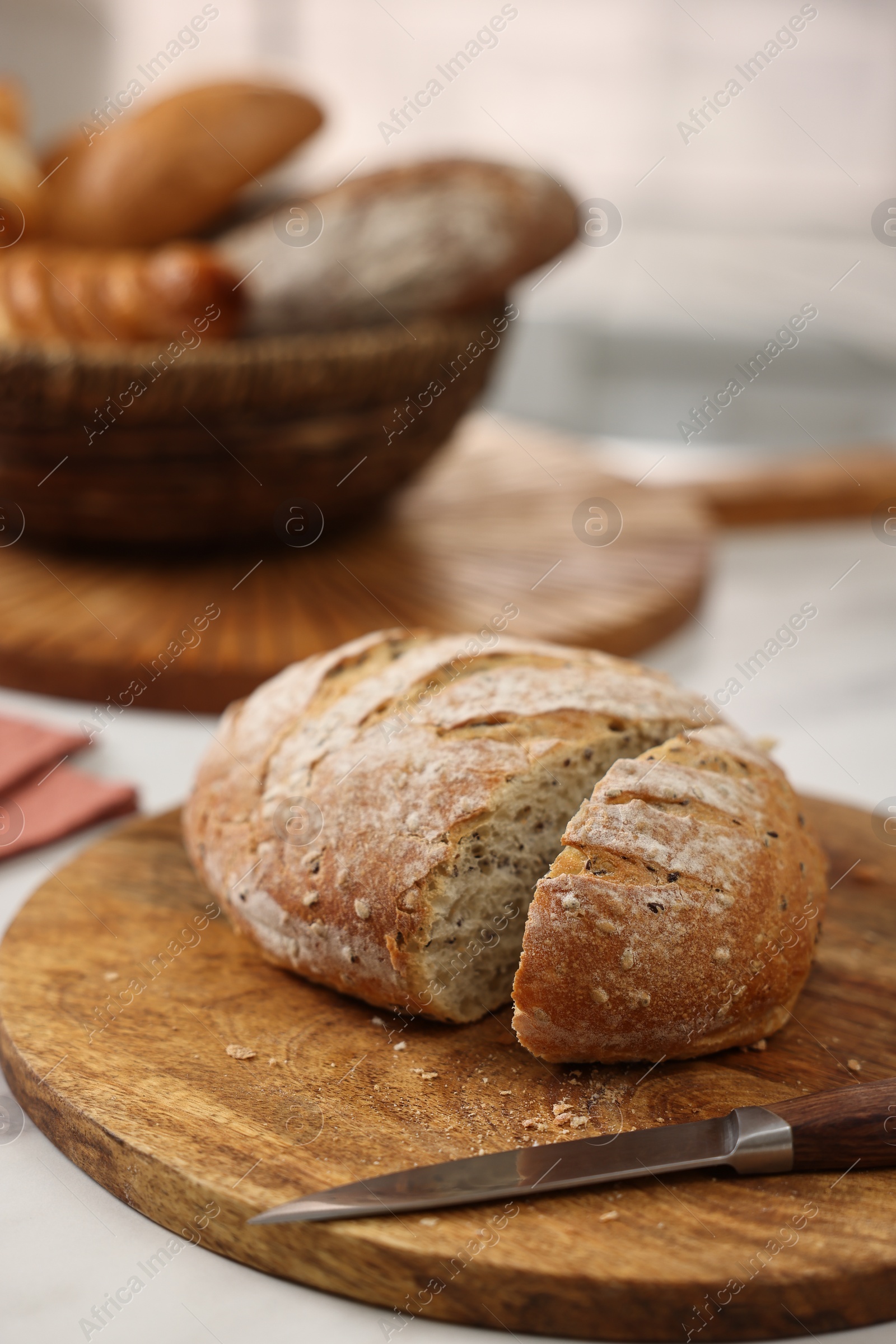 Photo of Wicker bread basket with freshly baked loaves and knife on white marble table in kitchen