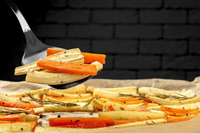 Taking baked parsnip and carrot with spatula from tray against brick wall, closeup