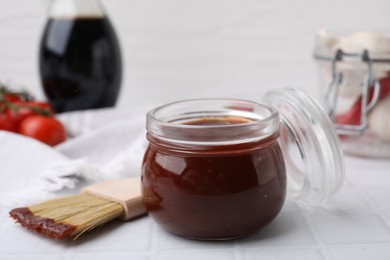 Photo of Marinade in jar and basting brush on white tiled table, closeup