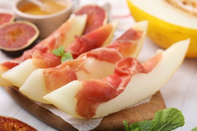 Photo of Tasty melon, jamon and figs served on wooden board, closeup