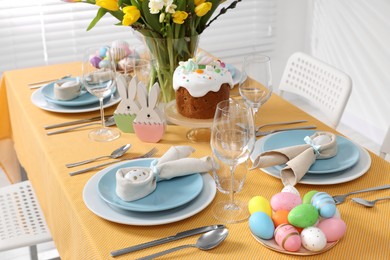Photo of Festive table setting with painted eggs, traditional Easter cake and vasetulips