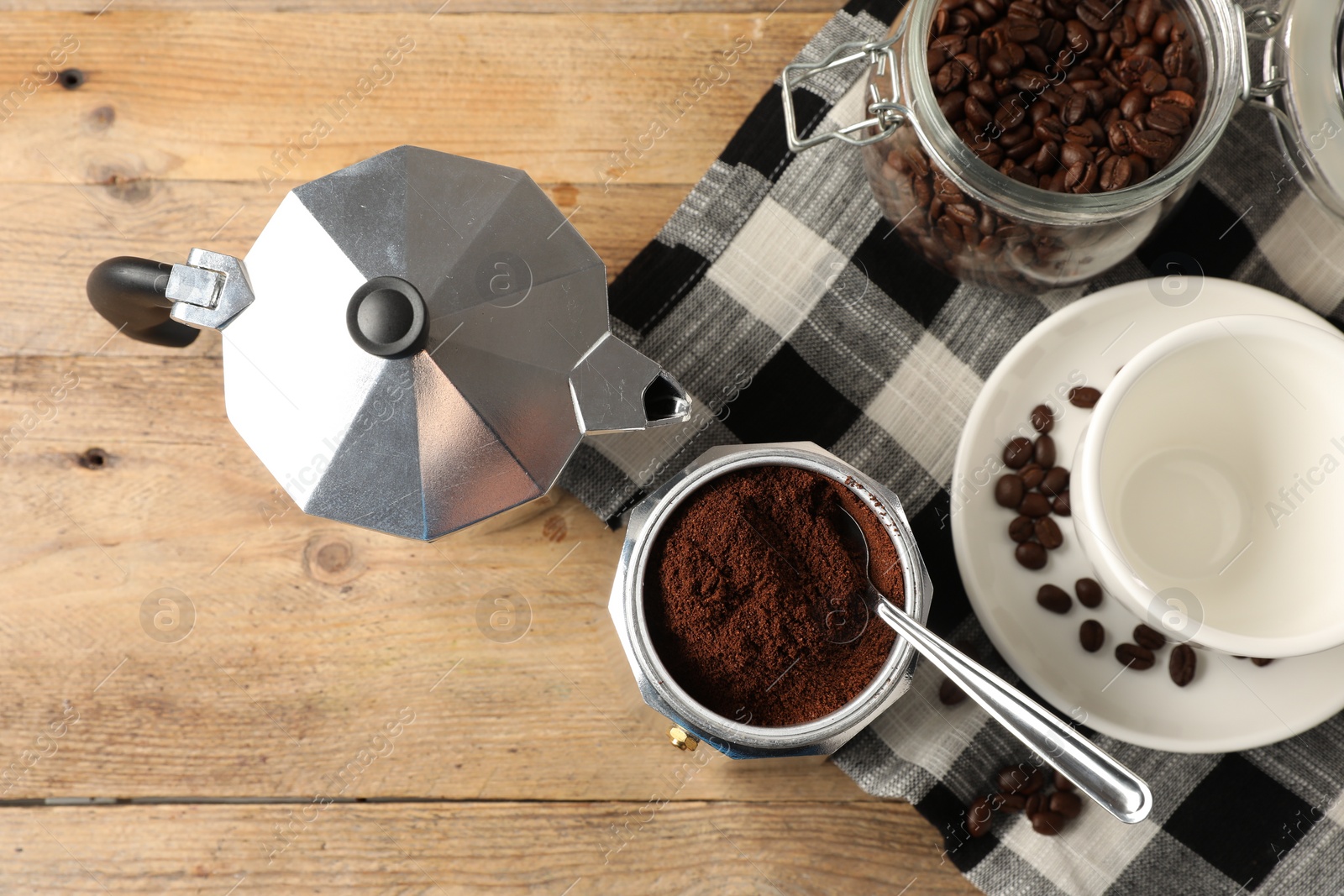 Photo of Moka pot with ground coffee, cup and beans on wooden table, flat lay