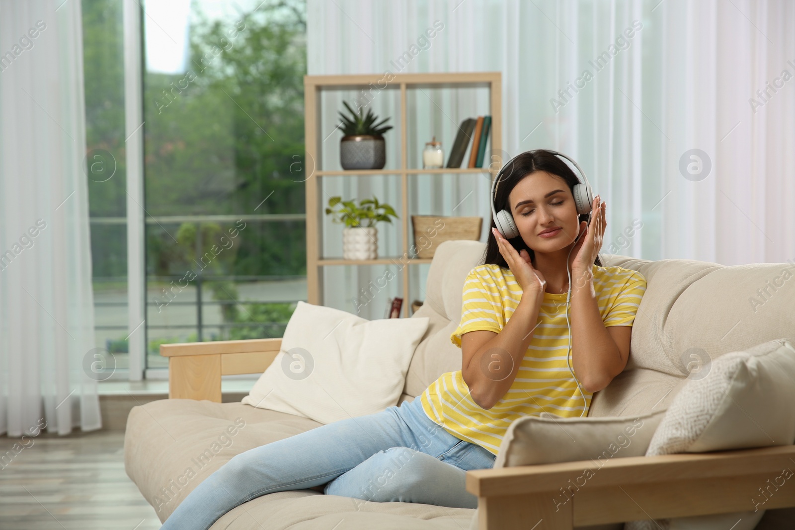 Photo of Young woman listening to music on sofa at home, space for text