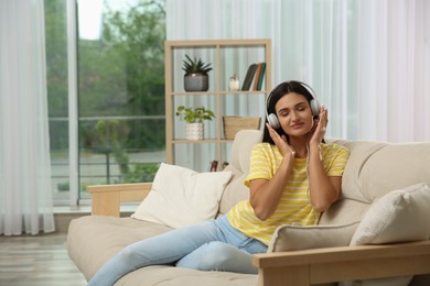 Photo of Young woman listening to music on sofa at home, space for text