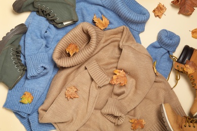 Photo of Flat lay composition with sweaters and dry leaves on beige background. Autumn season