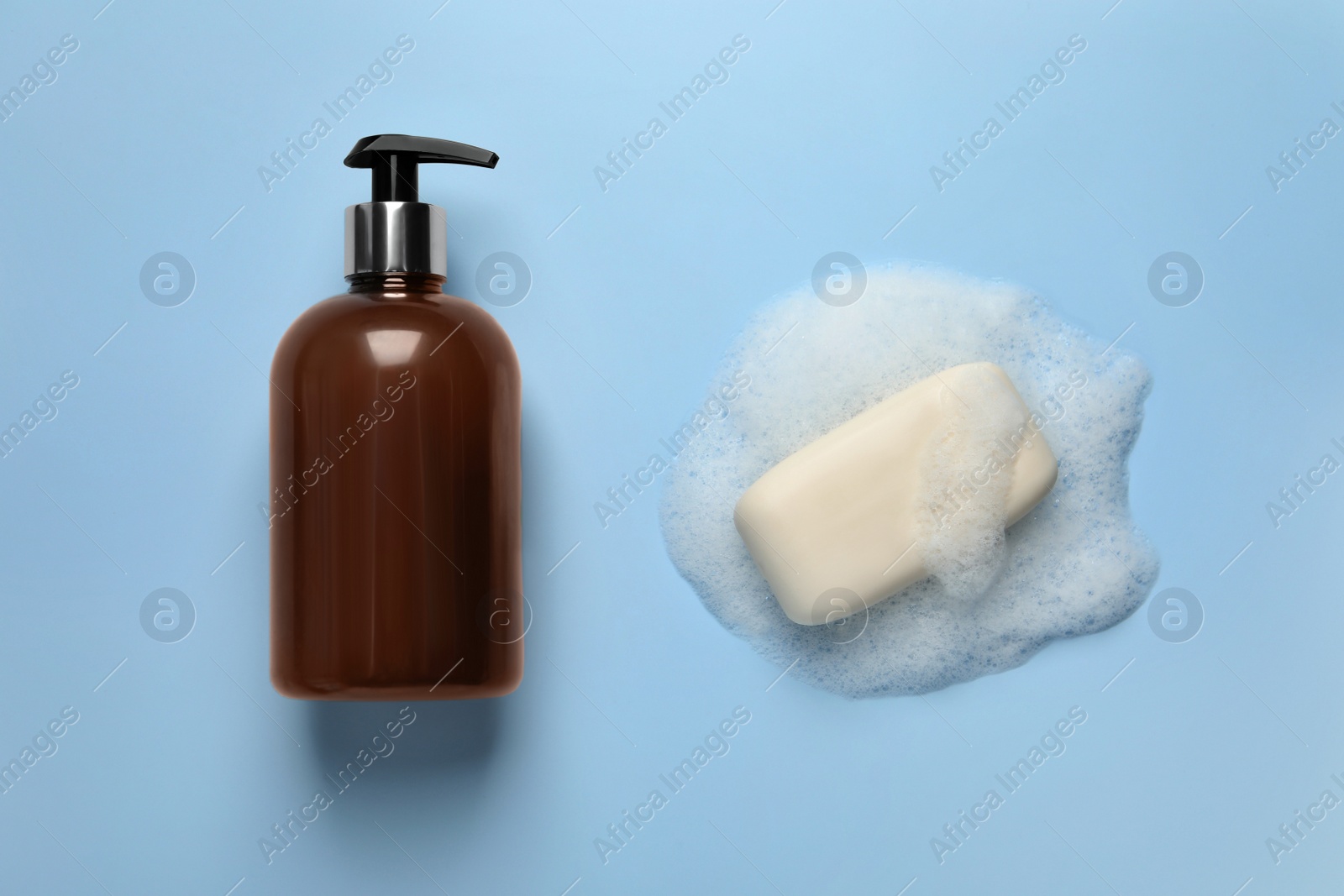 Photo of Dispenser and soap with fluffy foam on light blue background, top view