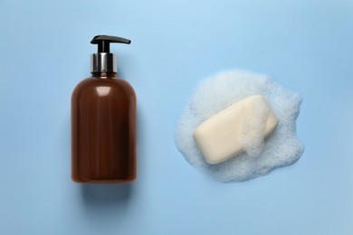 Dispenser and soap with fluffy foam on light blue background, top view