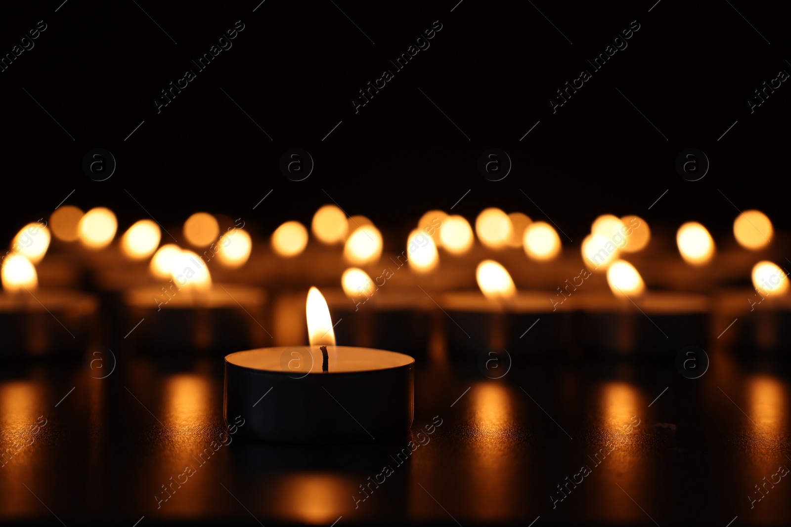 Photo of Burning candles on dark surface against black background, closeup