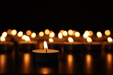 Photo of Burning candles on dark surface against black background, closeup