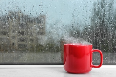 Photo of Cup of hot drink on windowsill, space for text. Rainy weather