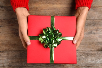 Photo of Woman holding Christmas gift at wooden table, top view