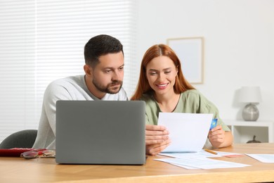 Photo of Couple with credit card using laptop for paying taxes online at home