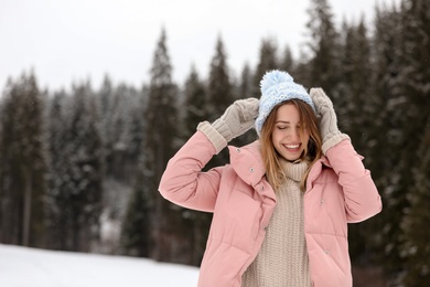 Photo of Young woman in warm clothes near forest, space for text. Winter vacation