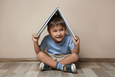Photo of Cute little boy with book on floor near beige wall