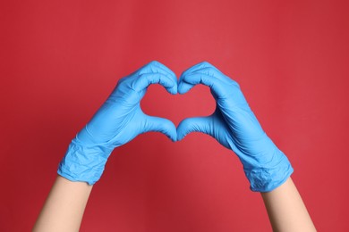 Photo of Doctor in medical gloves making heart with hands on red background, closeup