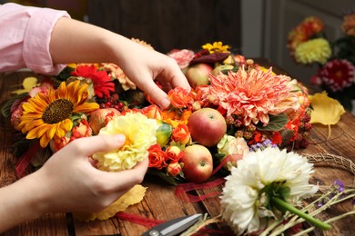 Photo of Florist making beautiful autumnal wreath with flowers and fruits at wooden table, closeup