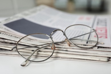 Stack of newspapers and glasses on white table, closeup