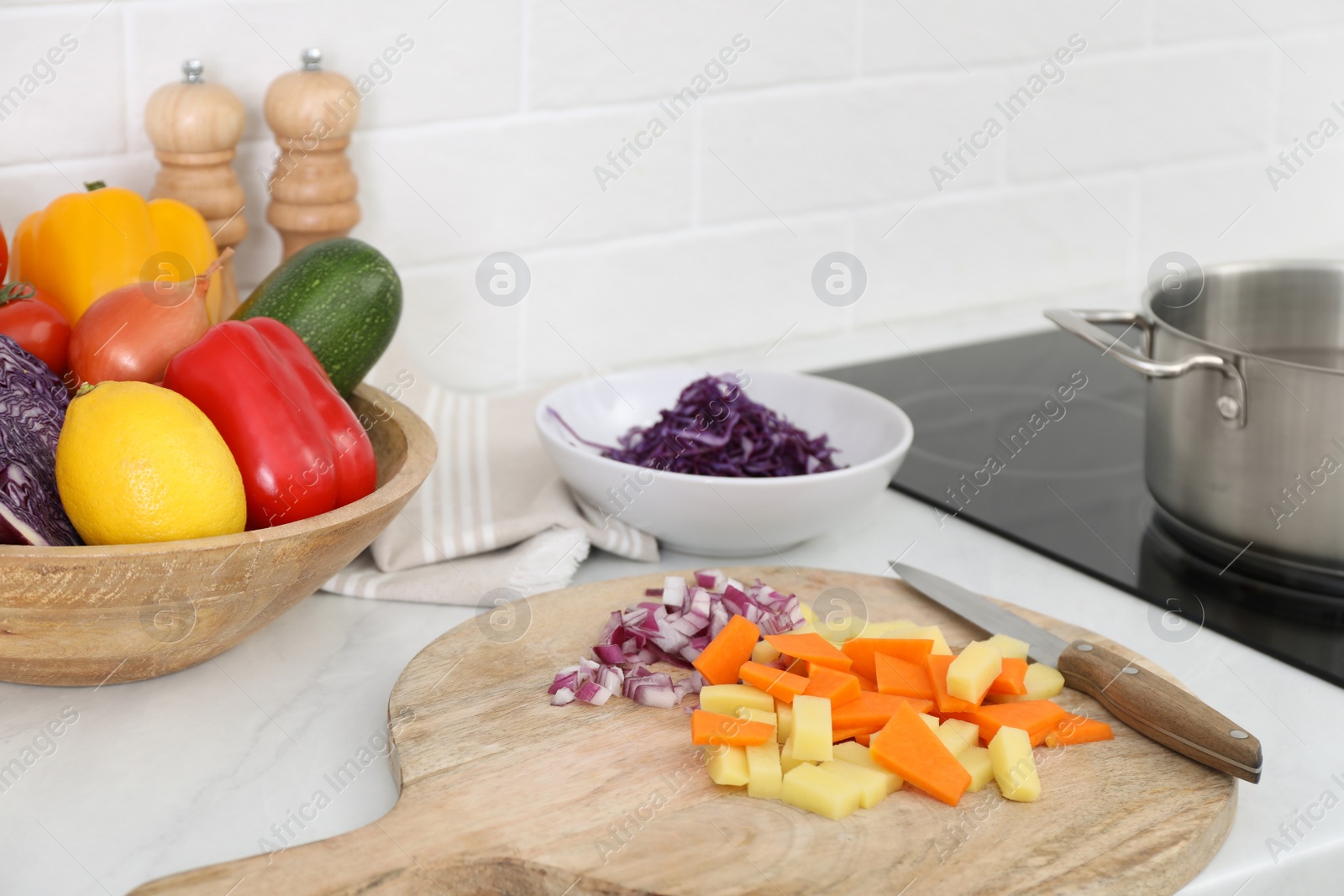 Photo of Board with cut vegetables and knife on white countertop in kitchen