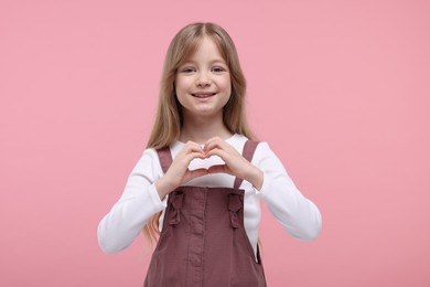 Photo of Happy girl showing heart gesture with hands on pink background