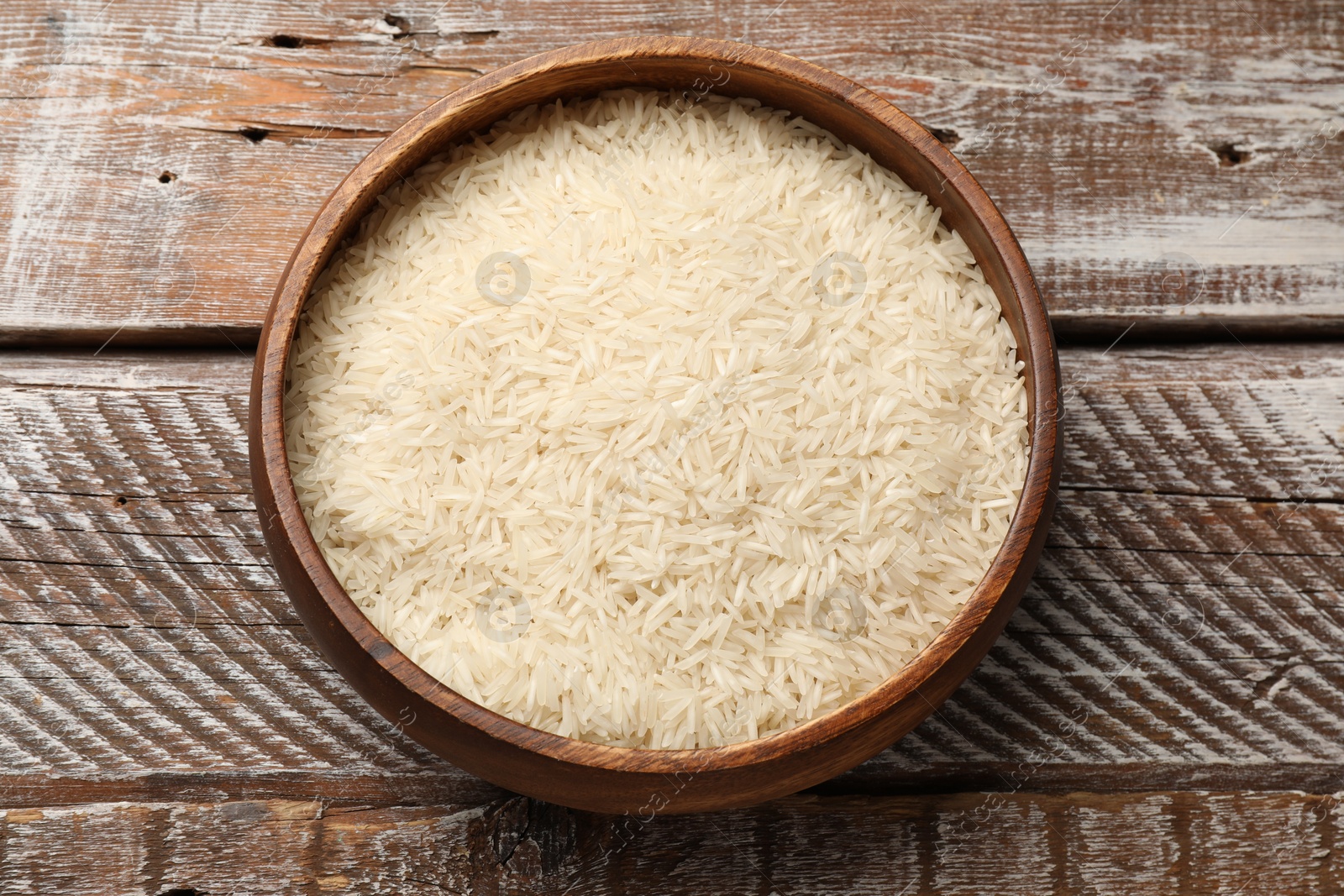 Photo of Raw basmati rice in bowl on wooden table, top view