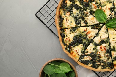 Delicious homemade quiche and fresh leaves on light gray table, flat lay. Space for text